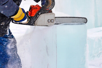A worker with a chainsaw in hand cuts the ice block. 
