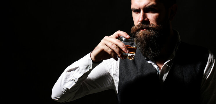Attractive man with a whiskey. Handsome bearded man with stylish hair mustache and beard drinking brandy or whiskey from glass
