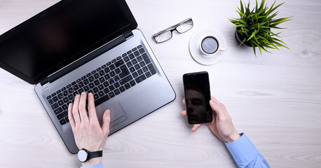 Businessman, man works at desktop on laptop and uses mobile phone. Top view, smartphone, glasses, cup of coffee. Mock up