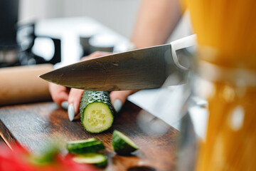 Unrecognizable woman cutting cucumber on wooden board close up