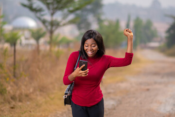 excited black lady rejoices as she checks her phone