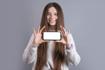 Happy attractive brunette woman girl in sweater showing hold blank phone smartphone screen. looking at the camera and smile over gray background