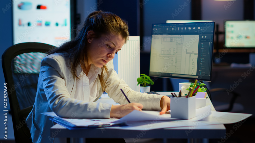 Poster overworked woman architect analysing and matching blueprints sitting at desk in front of computer la