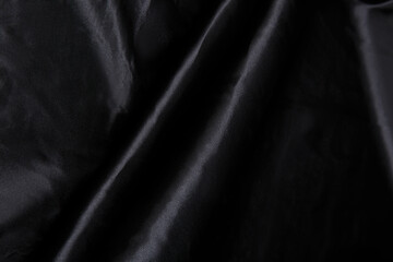 Colored black textile satin fabric folded in folds and waves with highlights and texture