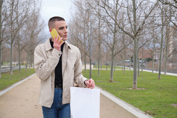 Handsome young man wearing make up, walking and speaking on his smartphone, carrying shopping bags. Non binary androgynous guy.