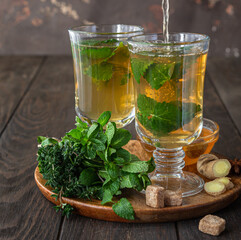 Process brewing tea. Hot herbal or mint tea with fresh herbs, ginger and honey, wooden background.