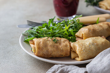 Homemade stuffed thin pancakes or crepes with meat, spicy cranberry sauce and arugula, light stone background. Traditional Russian cuisine for Maslenitsa. Shrove Tuesday.