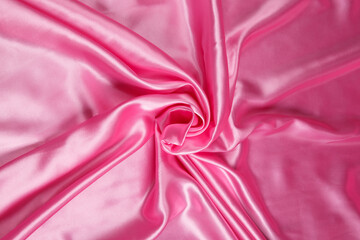 Colored pink textile satin fabric folded in folds and waves with highlights and texture
