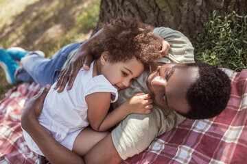 African american man hugging his cute little daughter and resting under the tree