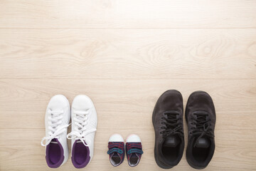 Father, mother and little kid sport shoes on wooden floor background. New family. Closeup. White female, black male and blue baby footwear. Empty place for text. Top down view.