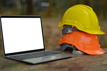 The laptop white screen is placed on the table next to the engineering hat.