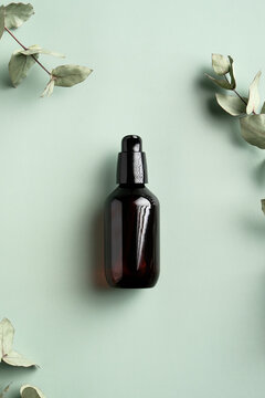 Dark amber glass bottle with serum and eucalyptus leaves on green background. Flat lay, top view. SPA natural organic cosmetics.