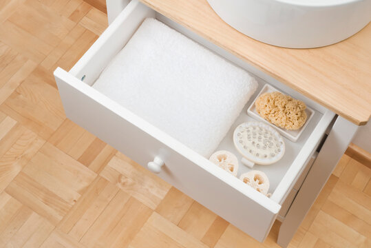 Open drawer under bathroom sink with towel and spa objects
