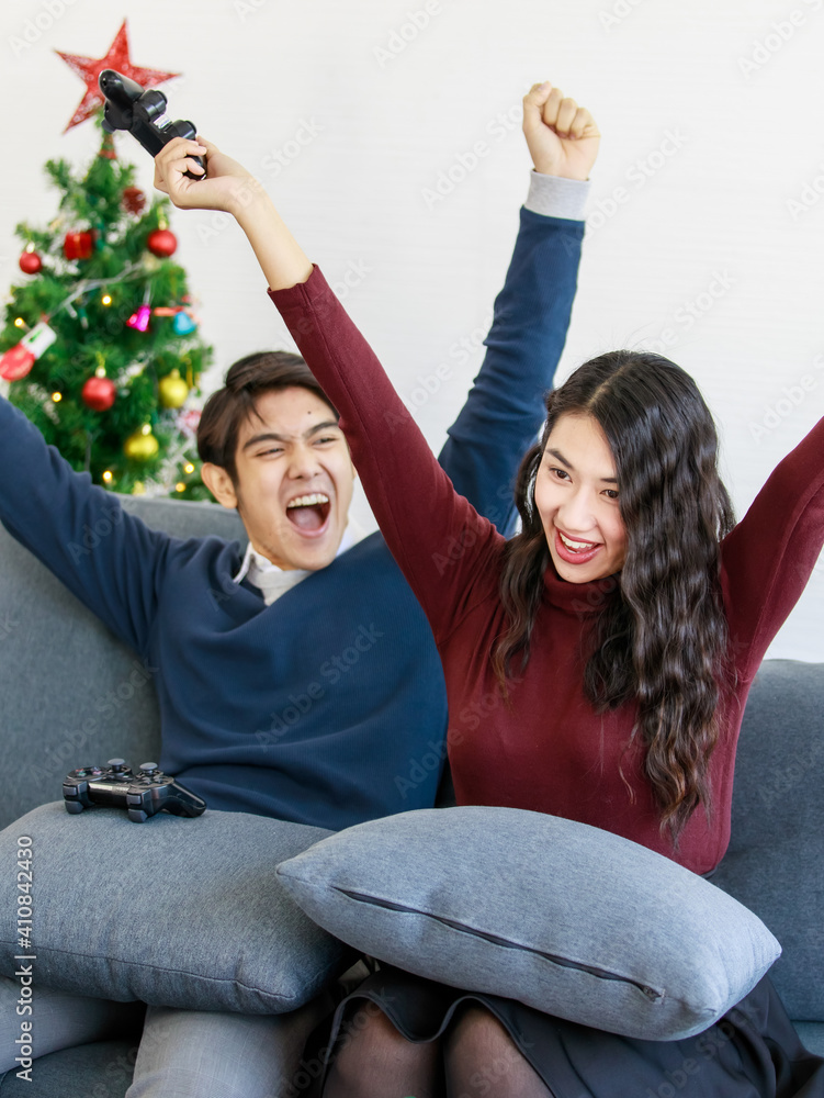 Wall mural portrait of cute smiling young asian lover couple having fun with playing a video game with console 