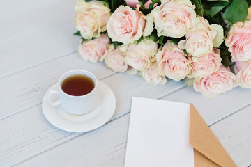 White blank card for text on a craft envelope with a bouquet of roses on a light background.