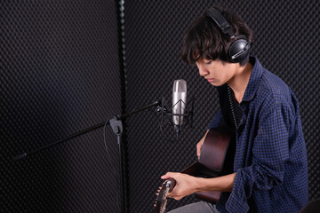 asian guy plaing acustic guitar in music studio record room