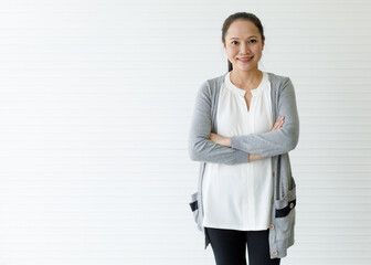 Medium shot portrait of a casual Asian woman with cute smiling in a white shirt under a gray cardigan and black pants with arm akimbo posing isolated with white background in the studio