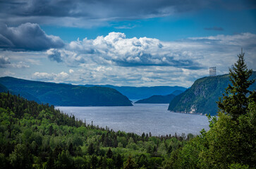 View point of fjord du Saguenay in Quebec Province on the East side with cloudy sky and windy weather. Green trees and grass on the foreground