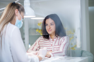 Nail artist in a mask doing manicure to the client