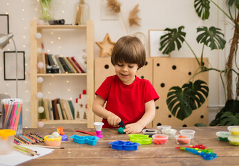 small boy in a red T-shirt plays with plasticine on a wooden table with stationery. Creative development of the child