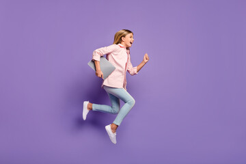 Full size profile photo of optimistic pretty girl jump run wear pink shirt jeans sneakers hold laptop isolated on violet background - obrazy, fototapety, plakaty