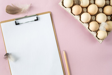 A box of organic fresh chicken eggs and a slipboard on a pink background. Eco-friendly egg production. Farming. Baking ingredients. View from above. Copy space. Horizontal.