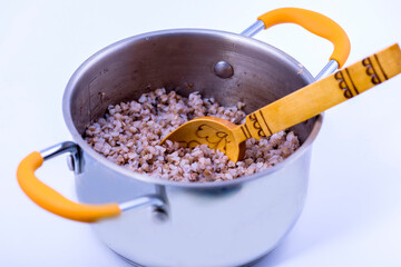 Buckwheat porridge in a saucepan with a wooden spoon on a white background.