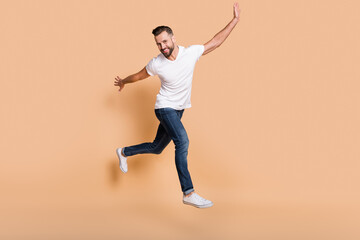 Fototapeta na wymiar Full length body size view of nice funky cheerful guy jumping having fun enjoying free time isolated over beige pastel color background