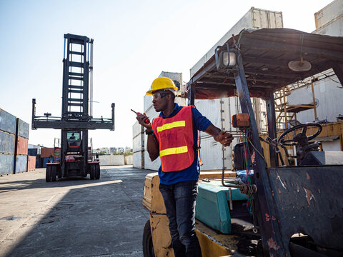 Foreman engineering african india hat yellow and red uniform safety warehouse site container cargo shipping.Male worker is call phone writing report import export investment manufacturing technology.