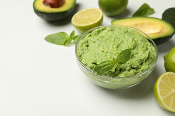 Bowl of guacamole, avocado, lime and basil on white background, space for text