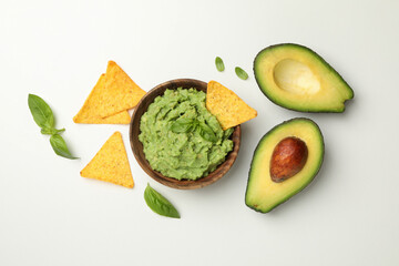 Bowl of guacamole, avocado, chips and basil on white background, top view