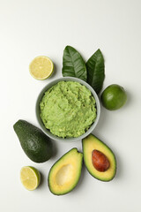 Bowl of guacamole, avocado and lime on white background, top view