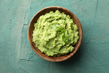 Bowl of guacamole on green textured background, top view