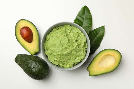 Bowl of guacamole and avocado on white background, top view