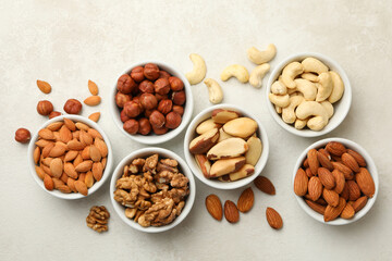 Bowls with different nuts on white textured background, top view