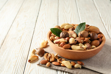 Bowl with different tasty nuts on white wooden background