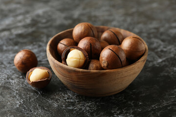 Bowl with tasty macadamia nuts on black smokey background