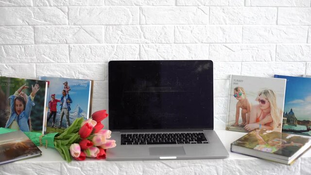 Laptop on white shelf with flowers. tulips, photo book.