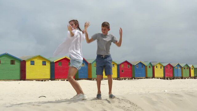Mother with son dancing on the white sands of South Africa near the colorful wood Muizenberg Beach Houses.