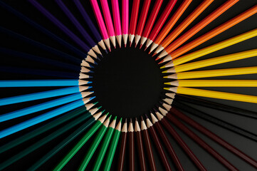 colored pencils laid out in a circle on a black background. top view