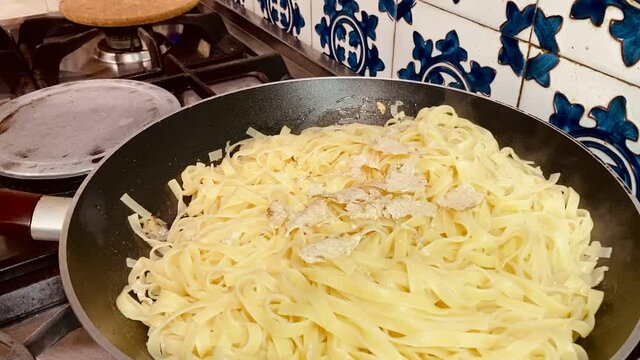 Sart&eacute;n con pasta y mano esparciendo trufa blanca