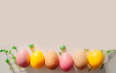 colored eggs of yellow, pink and beige presented on the white background with green sprouts as concept of spring and Easter