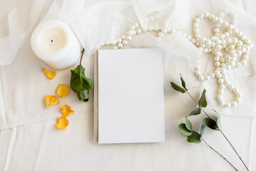 Fototapeta na wymiar Layout scene of a stationery layout. An empty vertical greeting card, a string of pearls and dried flowers isolated on a white table background. Top view blank for invitation