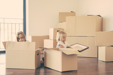 Fototapeta premium Focused little kids unpacking things in new apartment, sitting on floor and taking objects from open cartoon boxes. Relocation or moving concept