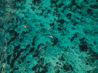 Naklejka na ściany i meble Aerial view with surfer paddle on surfboard in ocean.