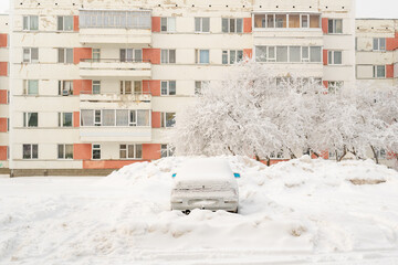 A car covered with snow in a parking lot in the courtyard of an apartment building. Russia