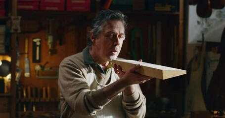 Cinematic shot of experienced master artisan luthier choosing fine quality wood for creation of handmade violin in creative workshop. Concept of spiritual instrument, art, orchestra, passion for music