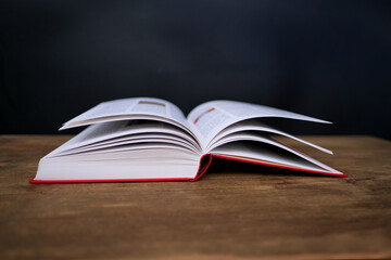 open paper book with red cover lies on a wooden table closeup, hand flipping pages, reading concept, copy space