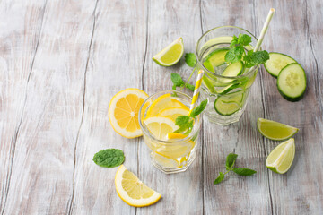Glasses with fresh lemon, cucumber, lime and mint on white wooden background, copy space.