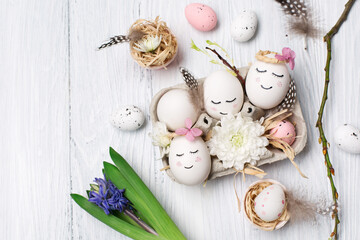 Zero waste Easter concept with white cute eggs, tree branches, quail feathers and spring flowers on white wooden background.